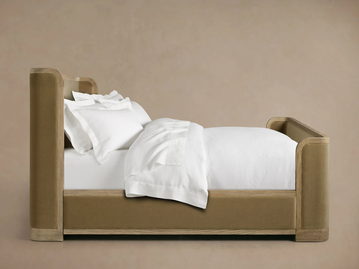 Curved corner of Darien Curved Shelter Bed's high footboard with oak veneer and upholstered tan paneling.