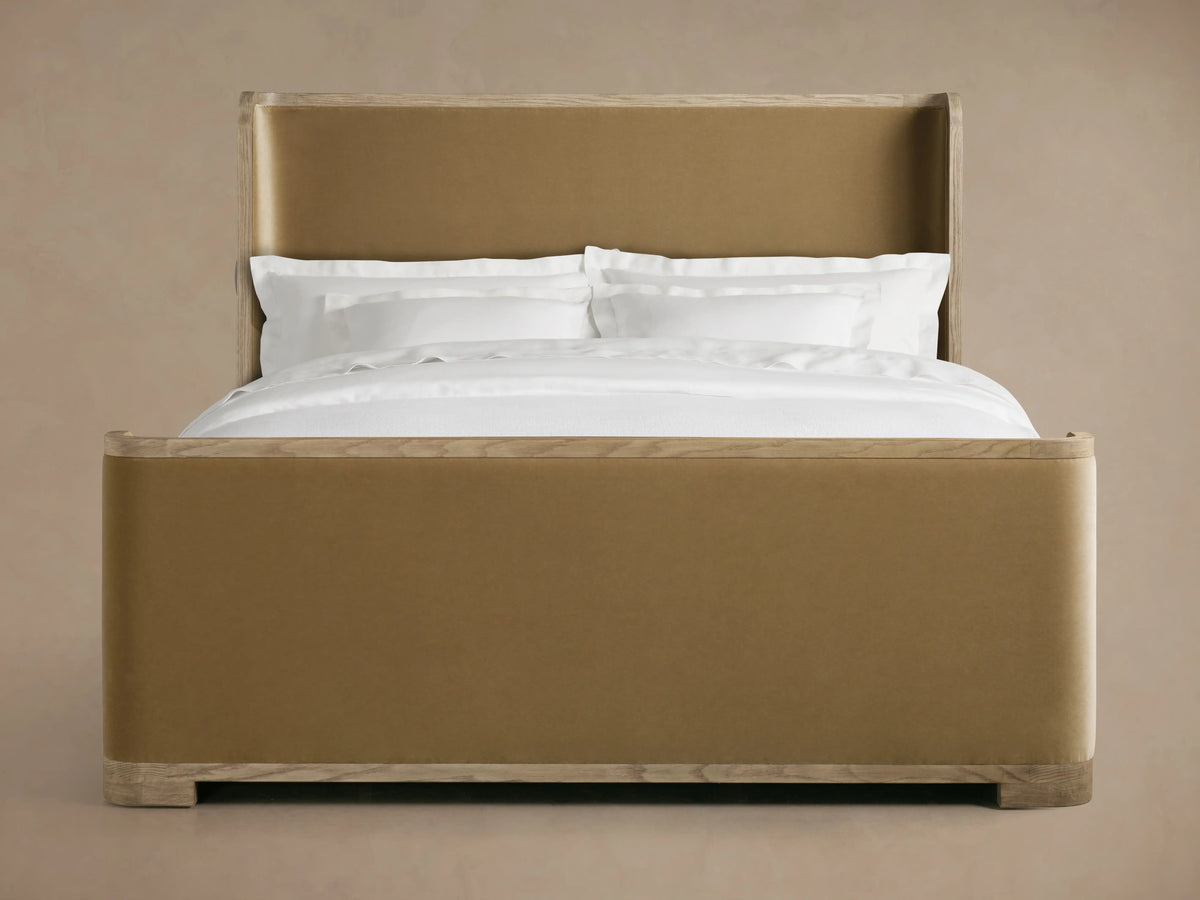 Darien Curved Shelter Bed with oak frame, upholstered panels, high footboard, and white bedding against a beige background.