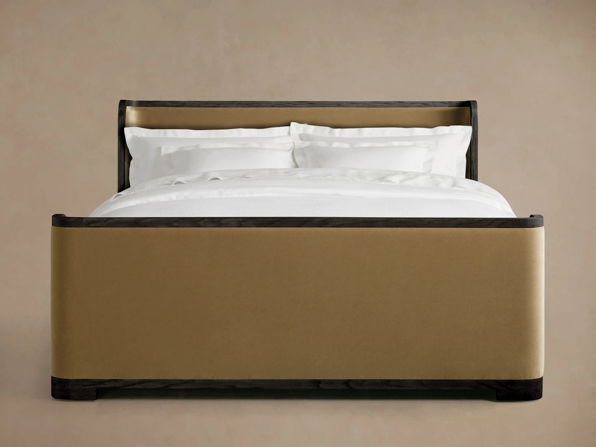 Alt text: Darien Curved Shelter Bed with a high footboard, framed in dark oak wood with tan upholstered panels, and white bedding.