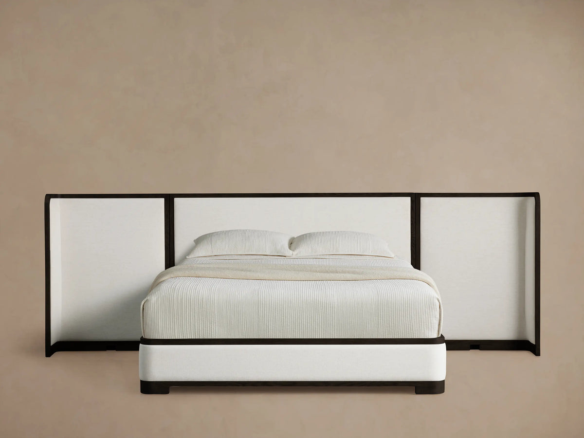 Darien Extended Curved Shelter Bed with white upholstered frame and a wide, dark-trimmed curved headboard, white bedding.