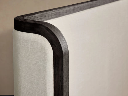 Darien Curved Shelter Bed with low footboard, oak veneer frame, upholstered panels, white bedding, against beige wall.