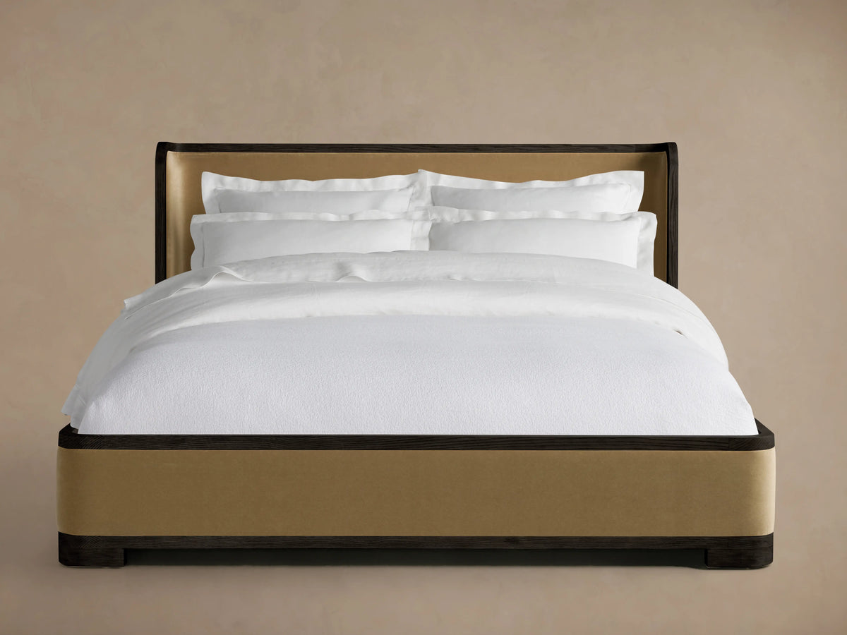 Darien Curved Shelter Bed with Low Footboard, oak frame, upholstered panels, white bedding, side view against beige background.