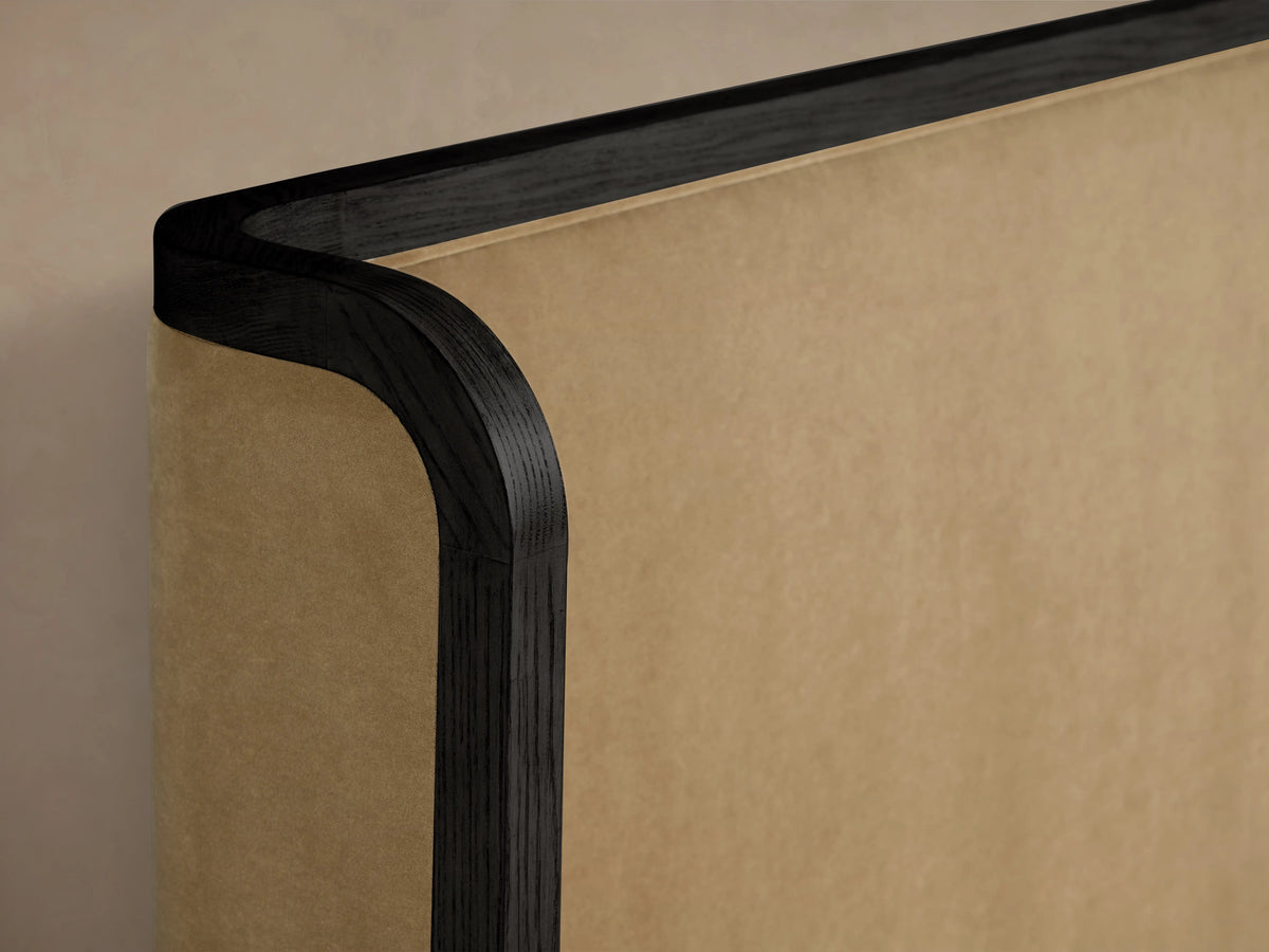 Curved corner of Darien Shelter Bed in oak wood with hand-applied finish, accented by beige upholstered panel, viewed close-up.