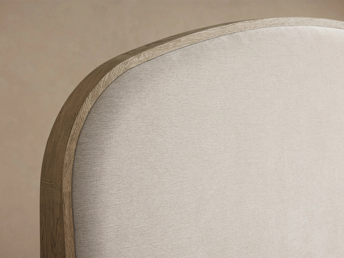 Danny Bed with light oak frame, curved neutral fabric headboard, and crisp white bedding, on a wooden floor.