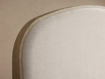 Danny Bed with light oak frame, curved neutral fabric headboard, and crisp white bedding, on a wooden floor.