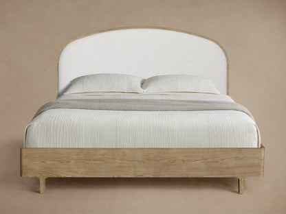 Danny Bed, angled view, light oak frame, curved white upholstered headboard, white striped bedding, grey throw.