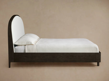 Close-up of Danny Bed headboard, showing a curved dark oak frame and textured off-white upholstered fabric.
