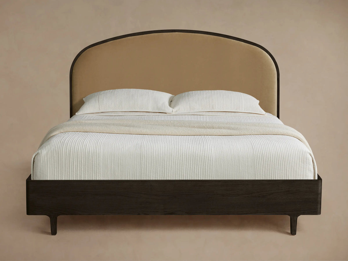 Curved tan upholstered headboard & dark wood frame Danny Bed with white ridged bedding & beige throw on wood floor.