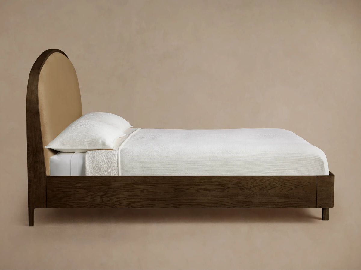 Front view of the Danny Bed with a dark wood frame, a curved beige upholstered headboard, and white bedding with a beige throw.