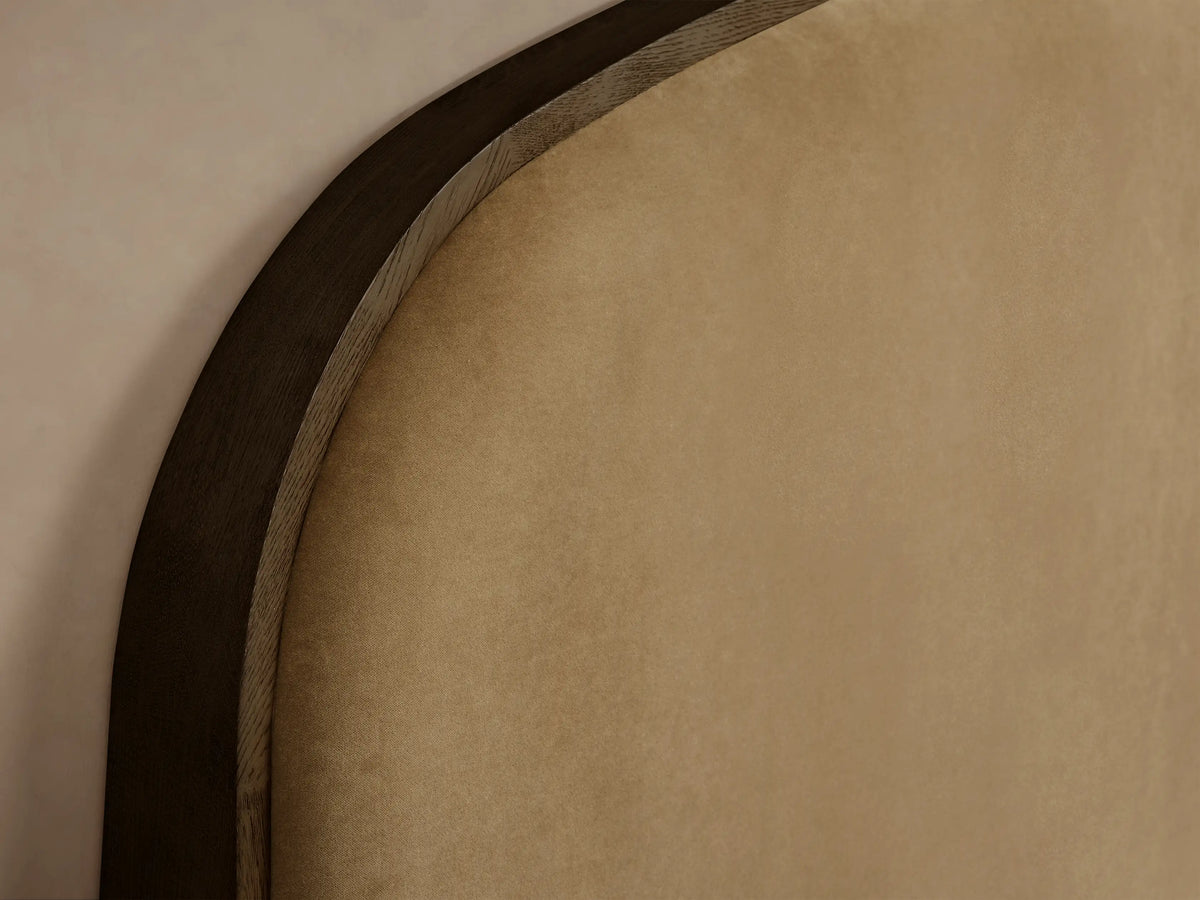 Close-up of the curved, dark oak wood frame and tan upholstered headboard of the Danny Bed.