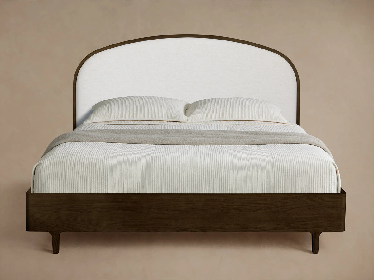 Front view of the Danny Bed with a dark wooden frame and an arched white upholstered headboard, styled with white bedding and a grey throw.