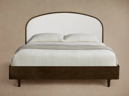 Front view of the Danny Bed with a dark wooden frame and an arched white upholstered headboard, styled with white bedding and a grey throw.