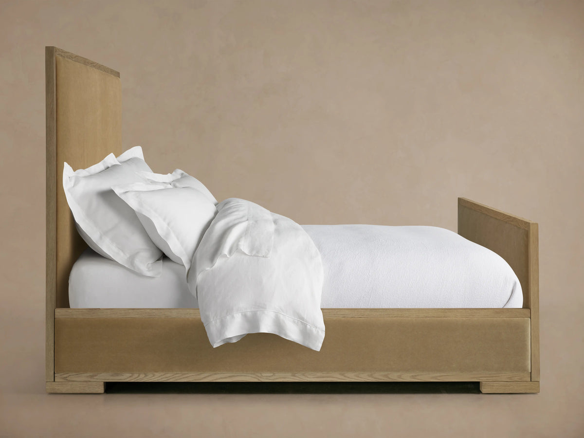 The Darien Panel Bed features a high footboard, oak wood frame, and upholstered panels. It is shown with white bedding.