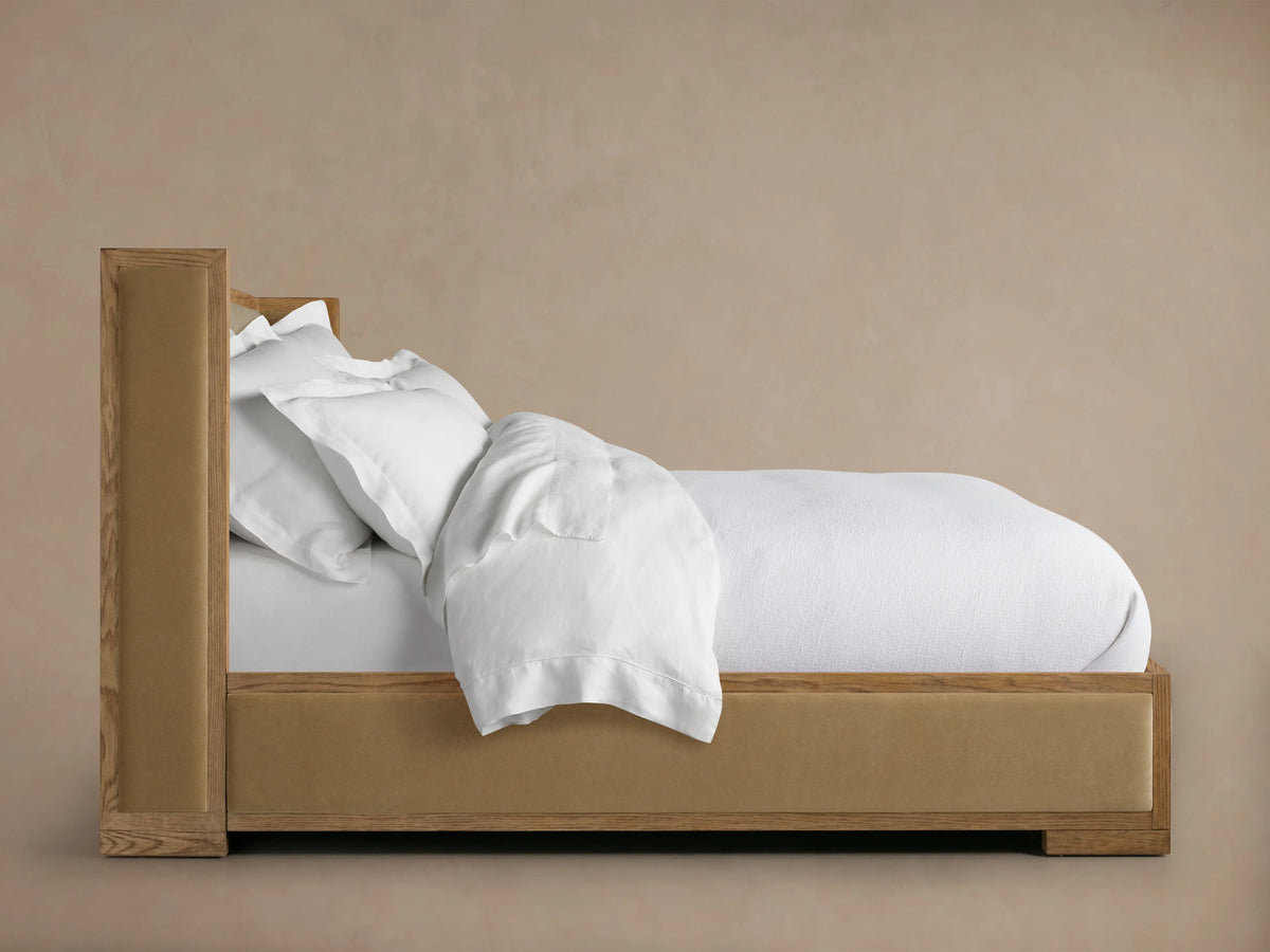 Close-up of Darien Shelter Bed's low footboard, showing oak wood frame with upholstered panel in a light brown finish.