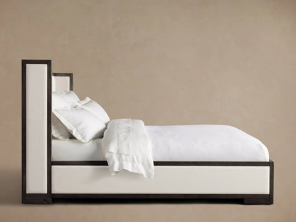 Darien Shelter Bed with Low Footboard in oak wood, upholstered panels, side view with white bedding and pillows, against beige background.