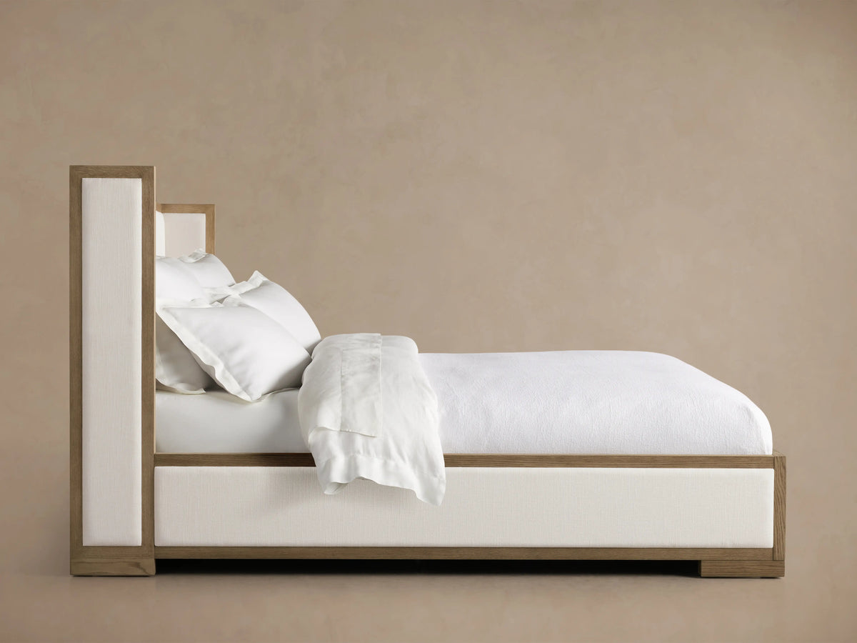 Darien Shelter Bed with white upholstered panels, low footboard, and dark oak frame on wooden floor in neutral room.