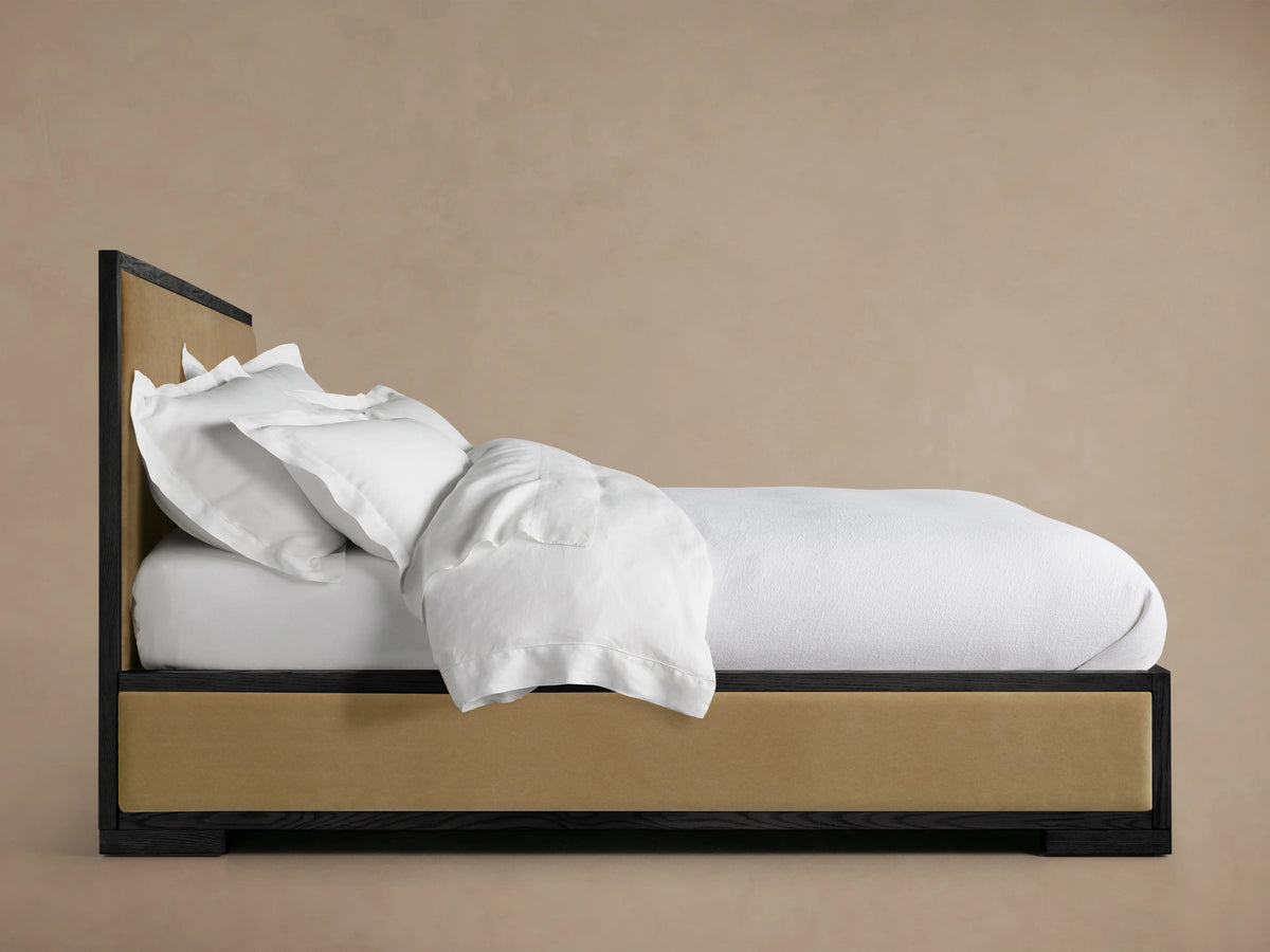 Darien Panel Bed with Low Footboard in oak, featuring upholstered panels. White bedding is styled messily on the mattress.
