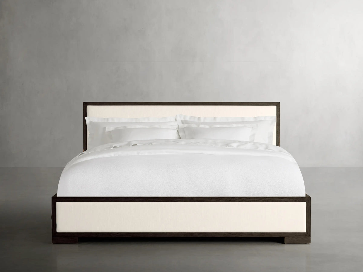 Darien Panel Bed with Low Footboard, oak frame with cream upholstered panels, white bedding, in a minimal room.