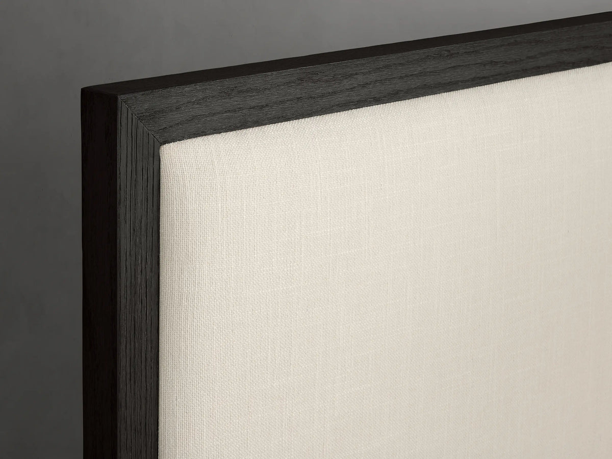 Darien Panel Bed with Low Footboard, dark oak frame, upholstered cream panels, white bedding, in minimalist room.