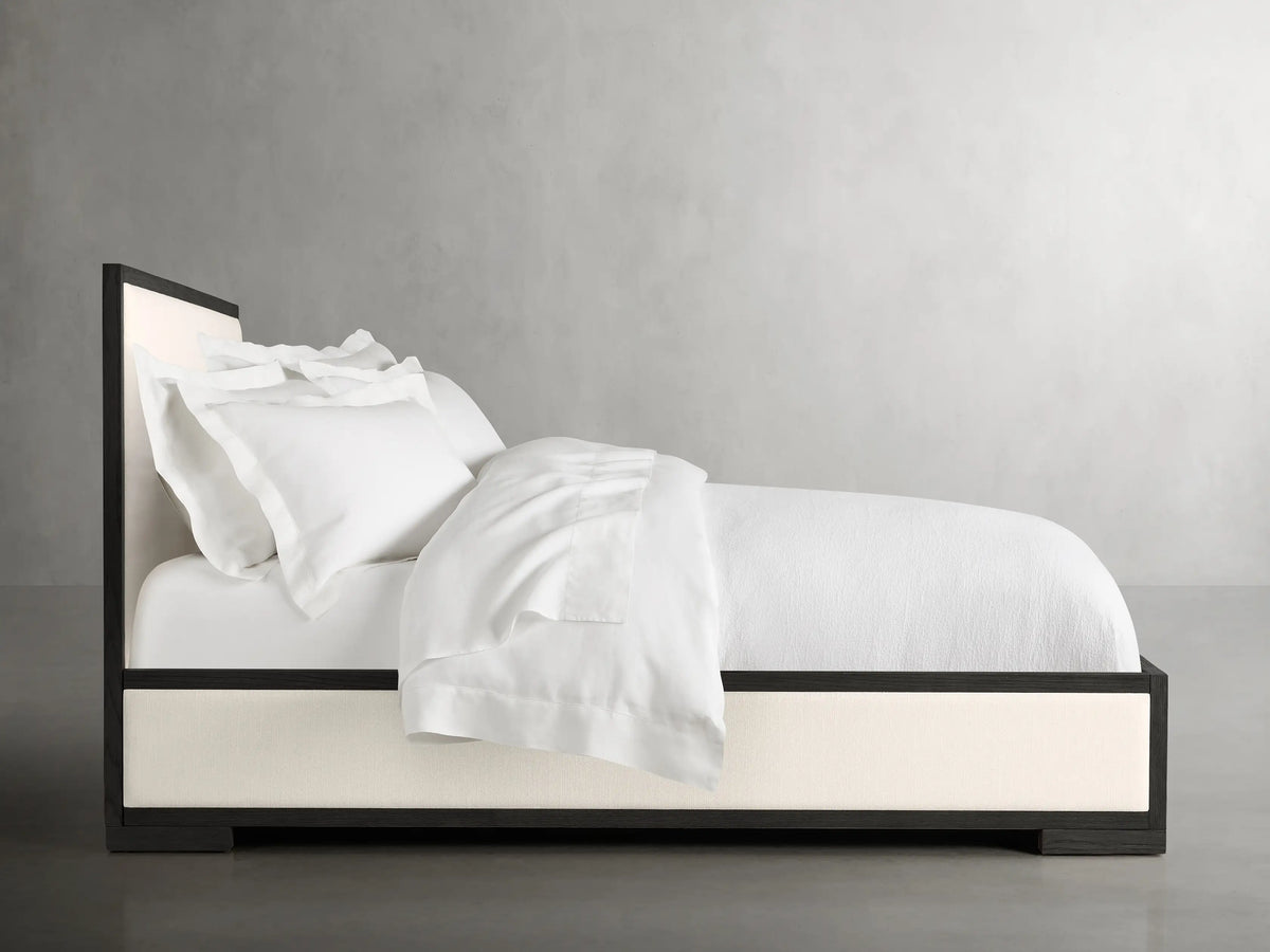 Alt text: Close-up of the Darien Panel Bed showcasing a dark oak frame with a cream upholstered panel.