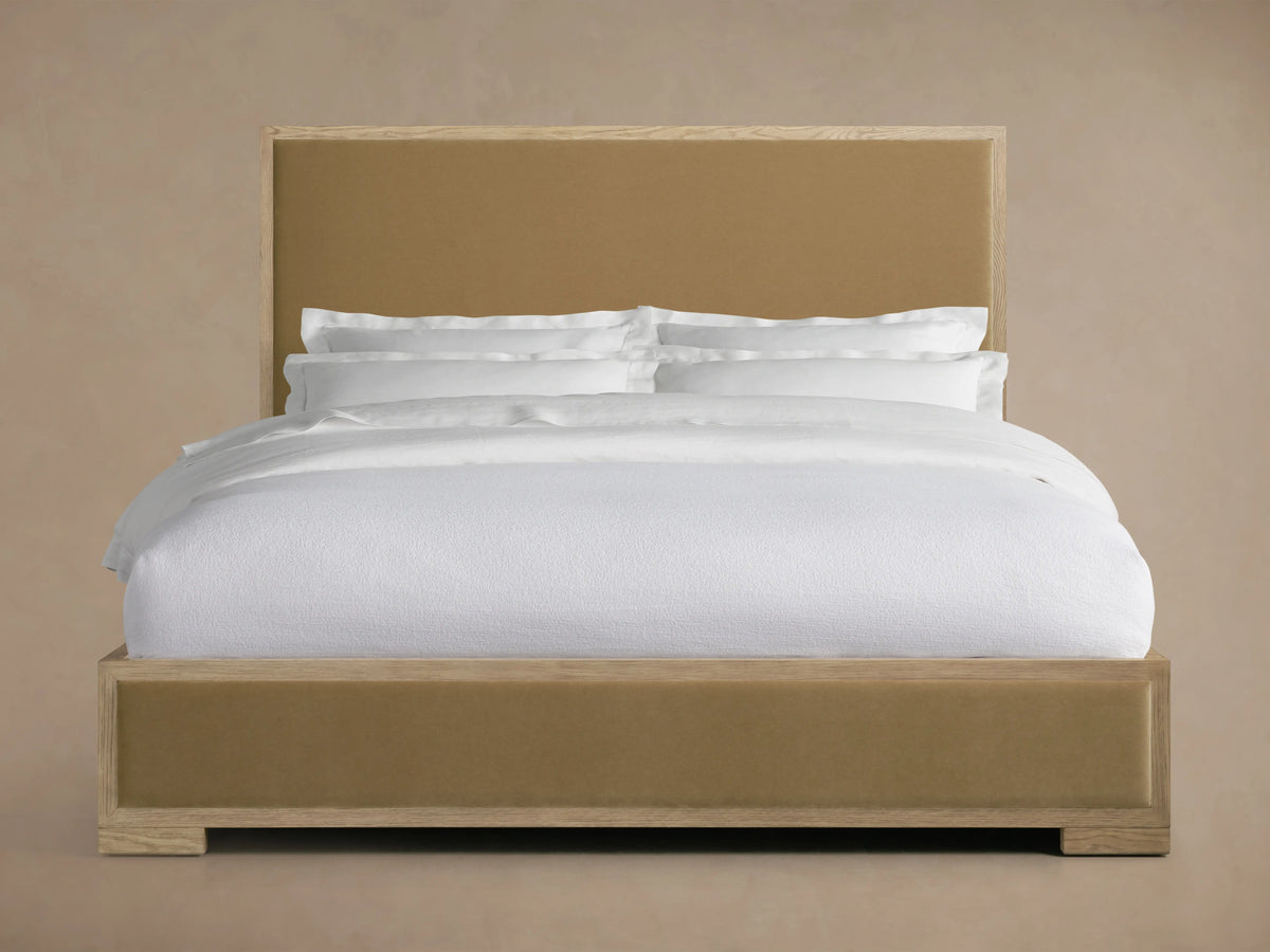 Bed with oak veneer and upholstered panels, featuring a low footboard. The headboard is tall and rectangular. Bedding is white.