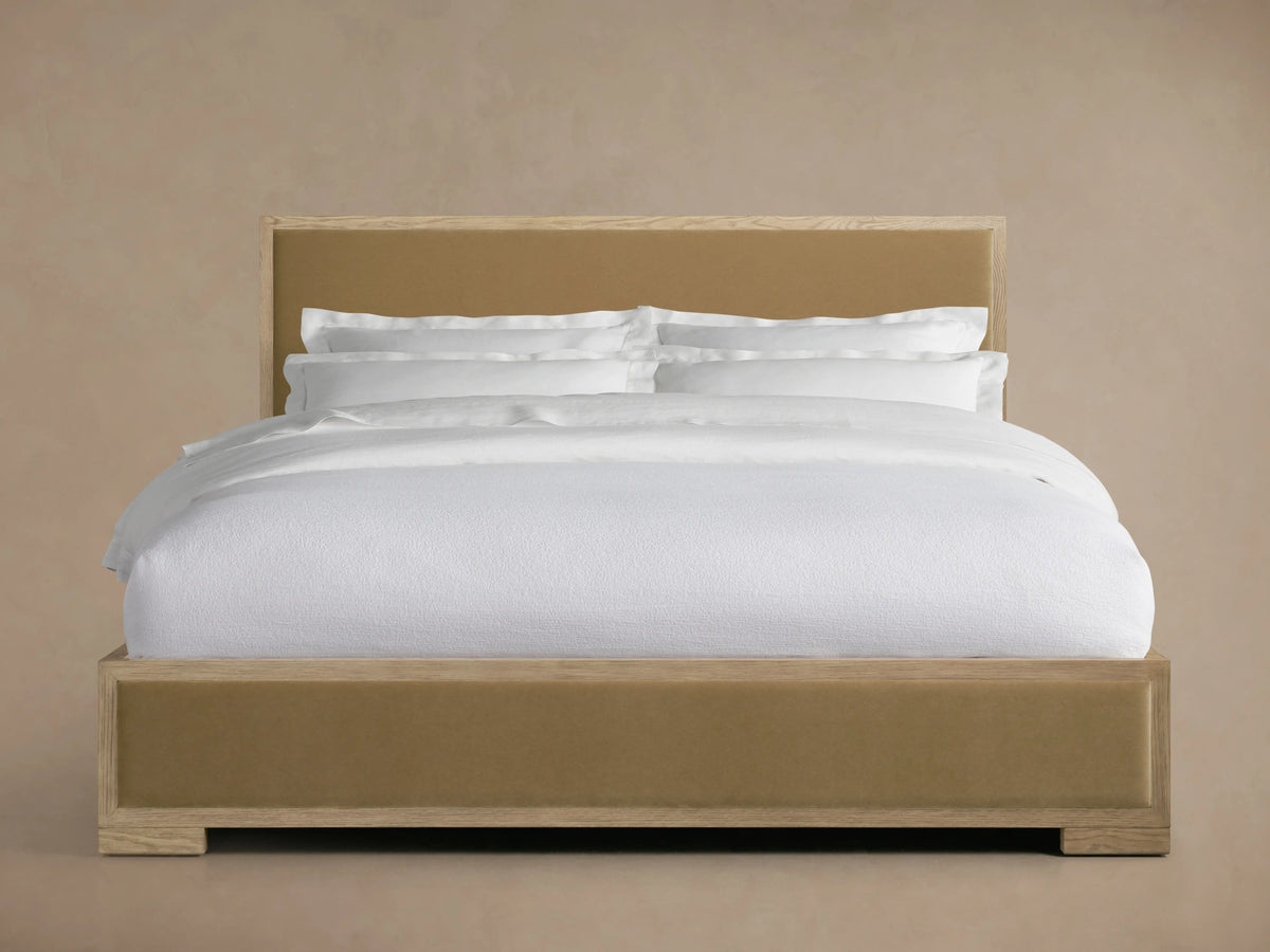 Darien Panel Bed with oak frame and upholstered panels. White bedding, low footboard. Set against a neutral background.