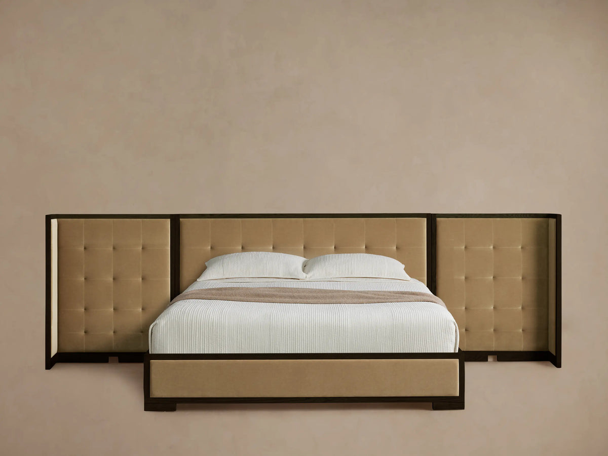 Darien Extended Box-Tufted Shelter Bed with dark brown frame and tan upholstered panels, white bedding, on wood floor.