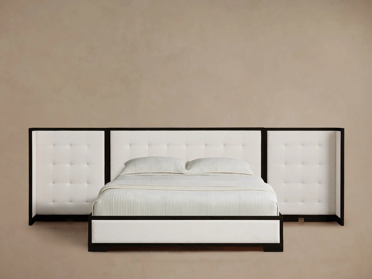Darien Extended Box-Tufted Shelter Bed with white tufted headboard and side wings, dark wood frame, white bedding, on wood floor.
