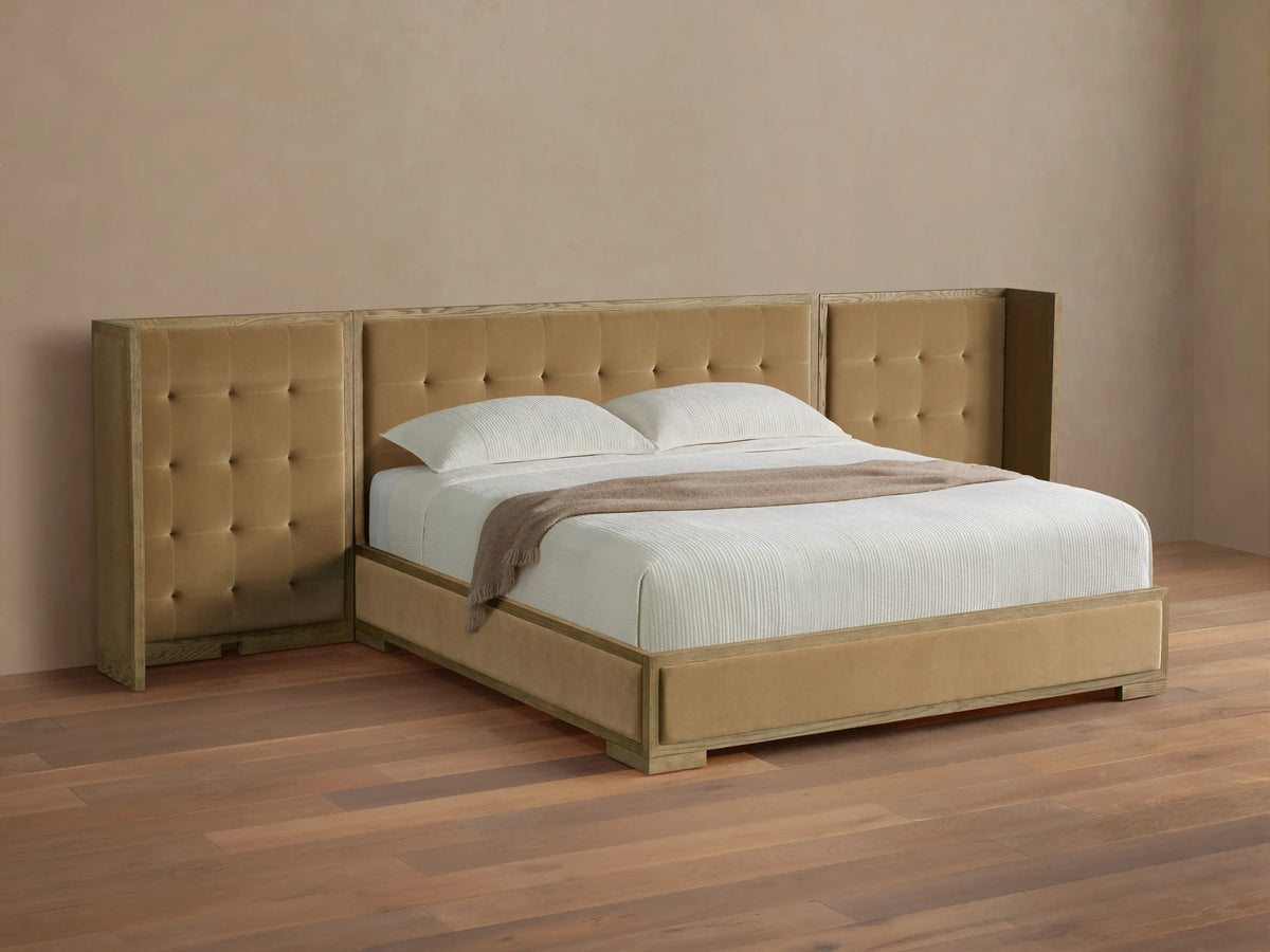 Darien extended shelter bed with light oak frame, camel box-tufted upholstery, white bedding, on a wood floor.