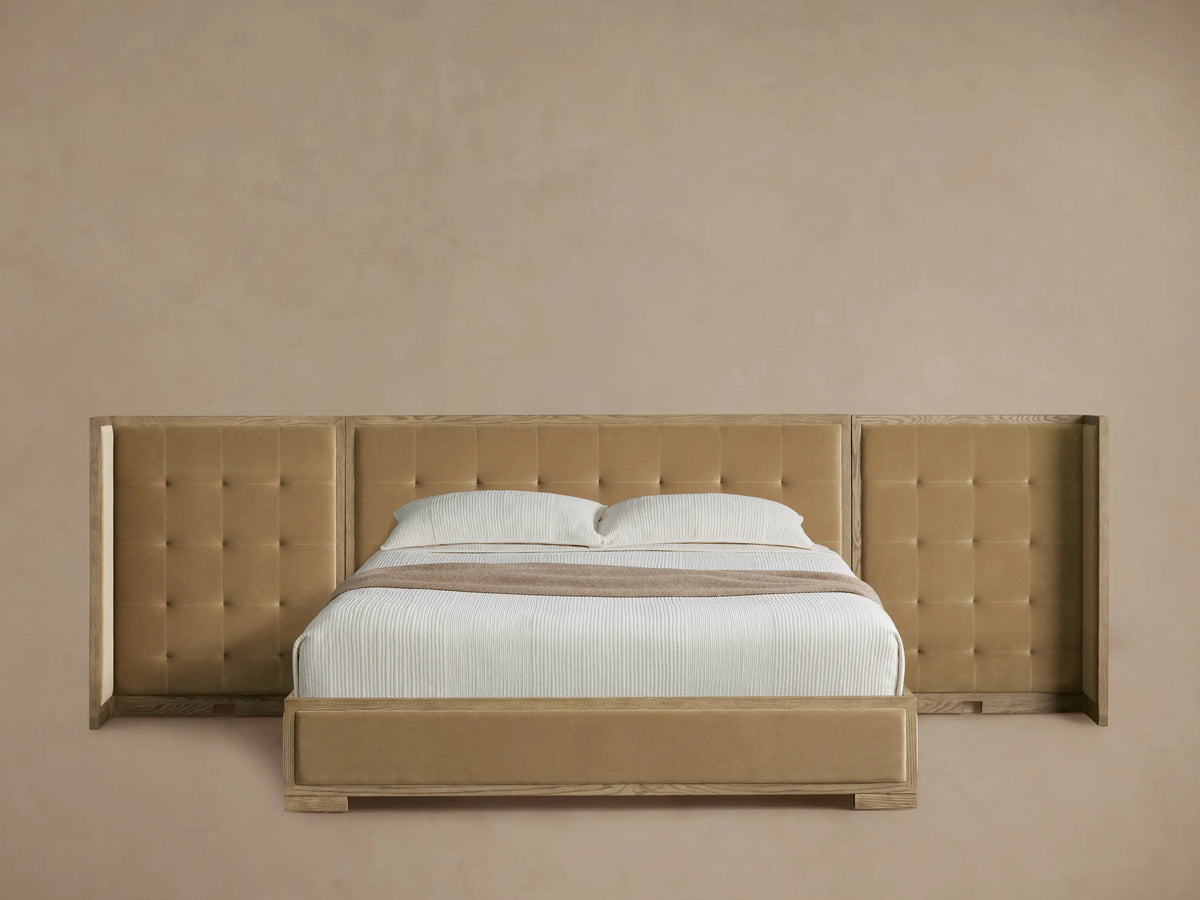 Darien extended shelter bed with light oak frame, camel box-tufted upholstery, white bedding, on a wood floor.