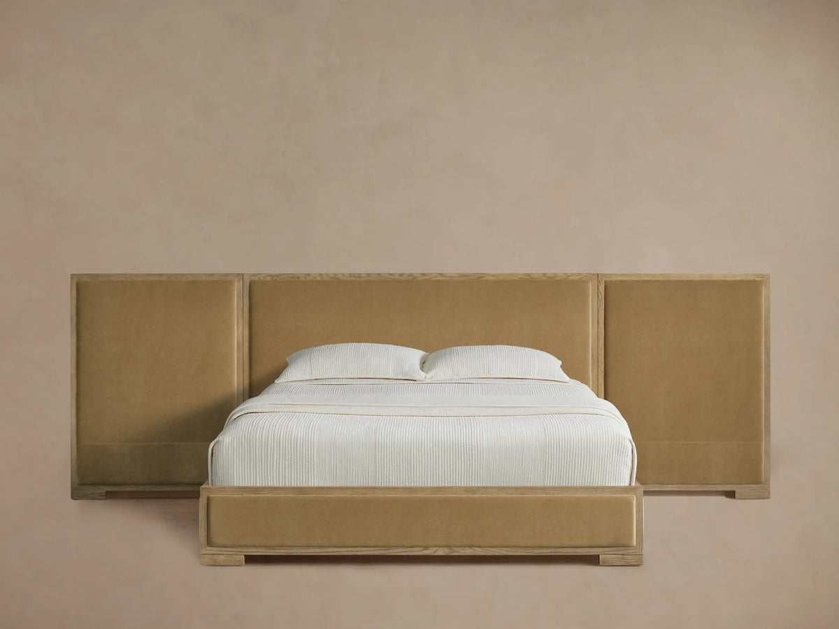 Darien Extended Panel Bed with oak frame, golden upholstered extended headboard panels, white bedding, on a wood floor.