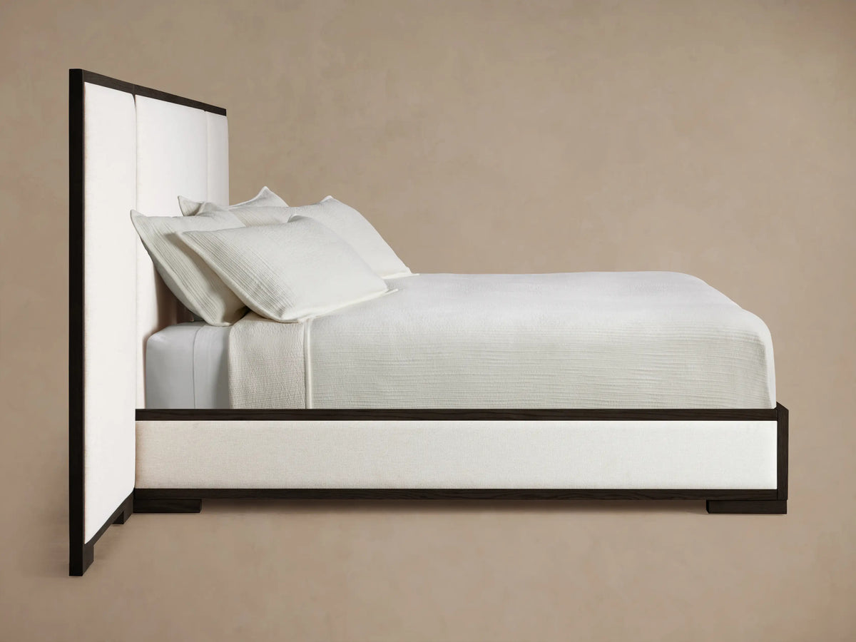 Close-up of Darien Extended Panel Bed headboard corner. Dark oak frame with visible grain, framing an off-white upholstered panel.