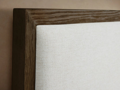 Side profile of the Darien Extended Panel Bed, featuring a dark oak frame, white upholstered headboard panels, and white bedding.
