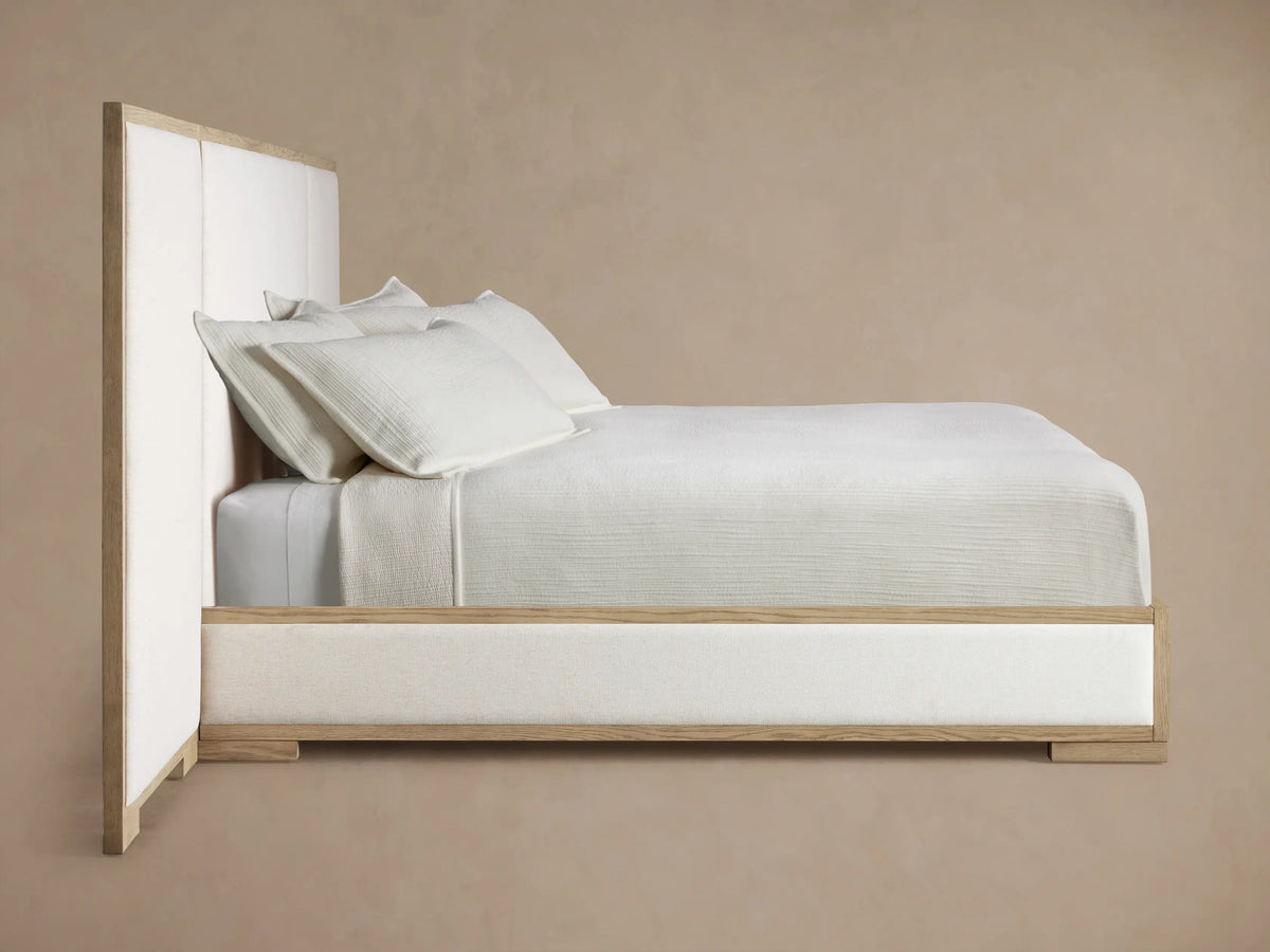 Close-up of Darien Extended Panel Bed's light oak frame with visible grain and a textured, off-white upholstered panel.