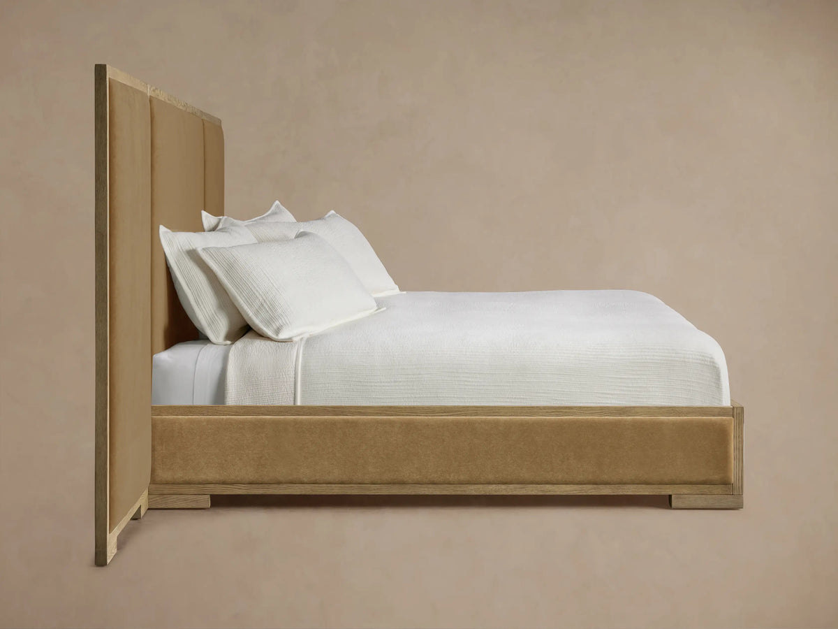 Darien Extended Panel Bed. Close-up of light oak frame with visible grain around a plush, tan upholstered headboard panel.