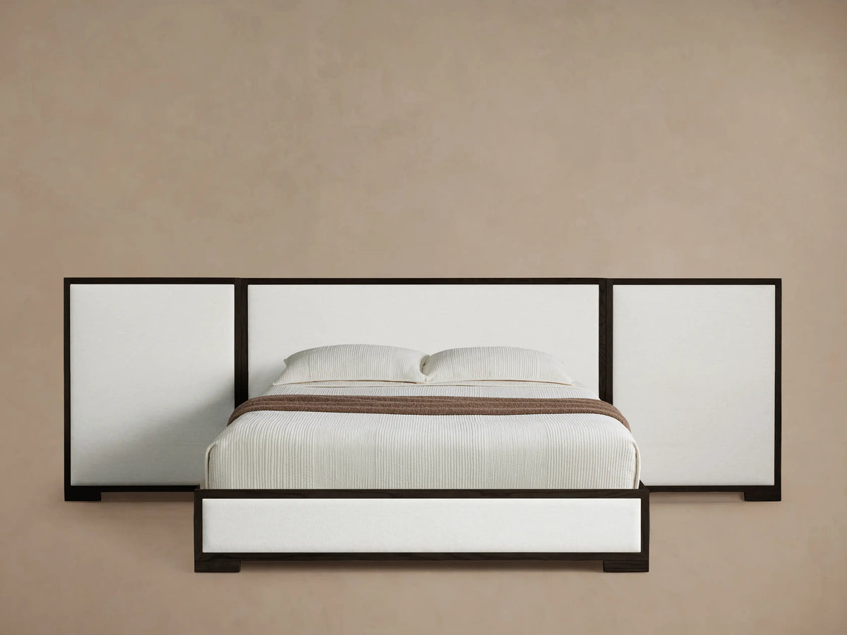 Darien Extended Panel Bed with dark wood frame, white upholstered panels, extended headboard, white bedding, and brown throw.