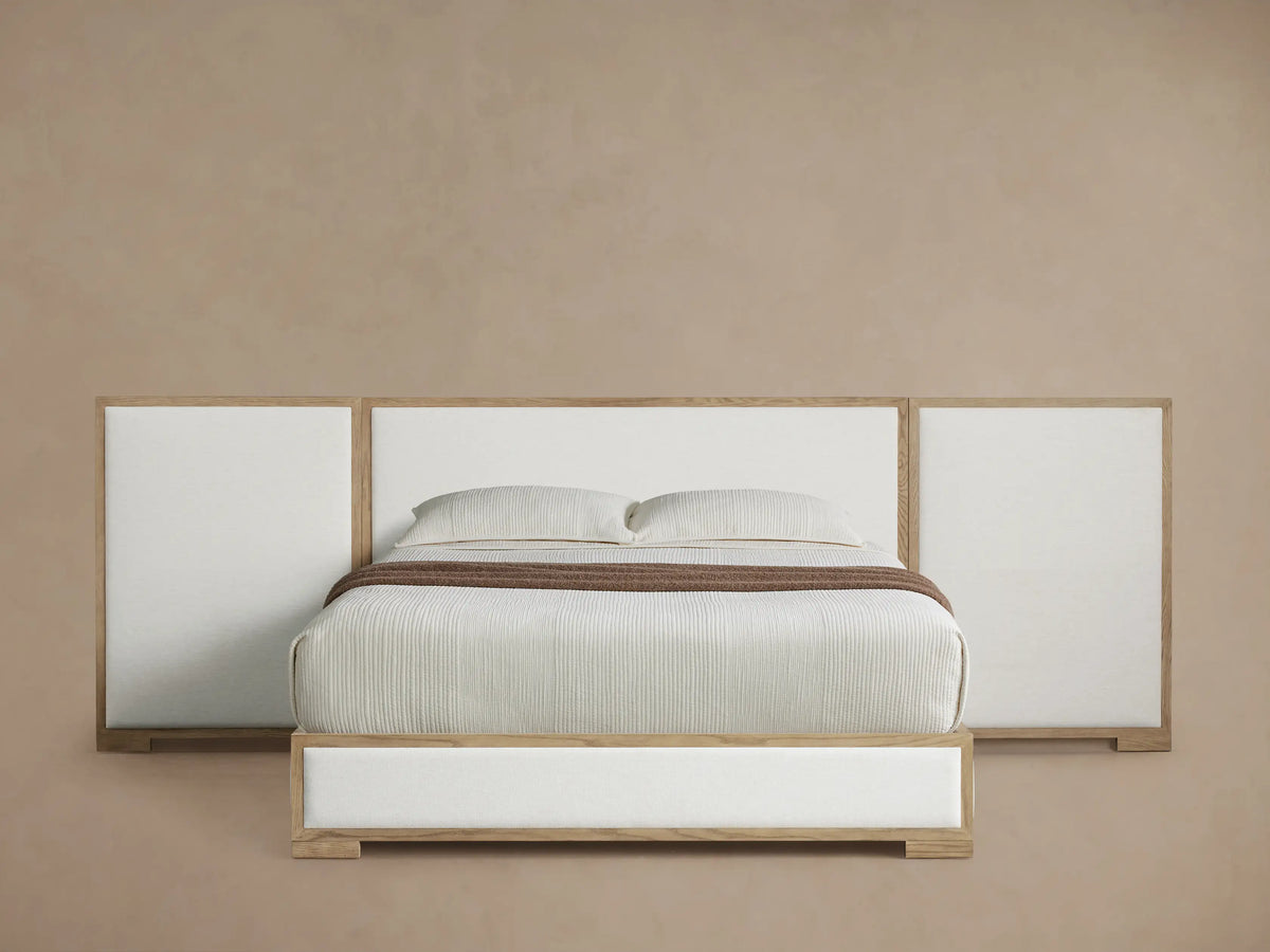 Darien Extended Panel Bed: light oak frame, white upholstered extended headboard & base, white bedding, brown throw on wood floor.