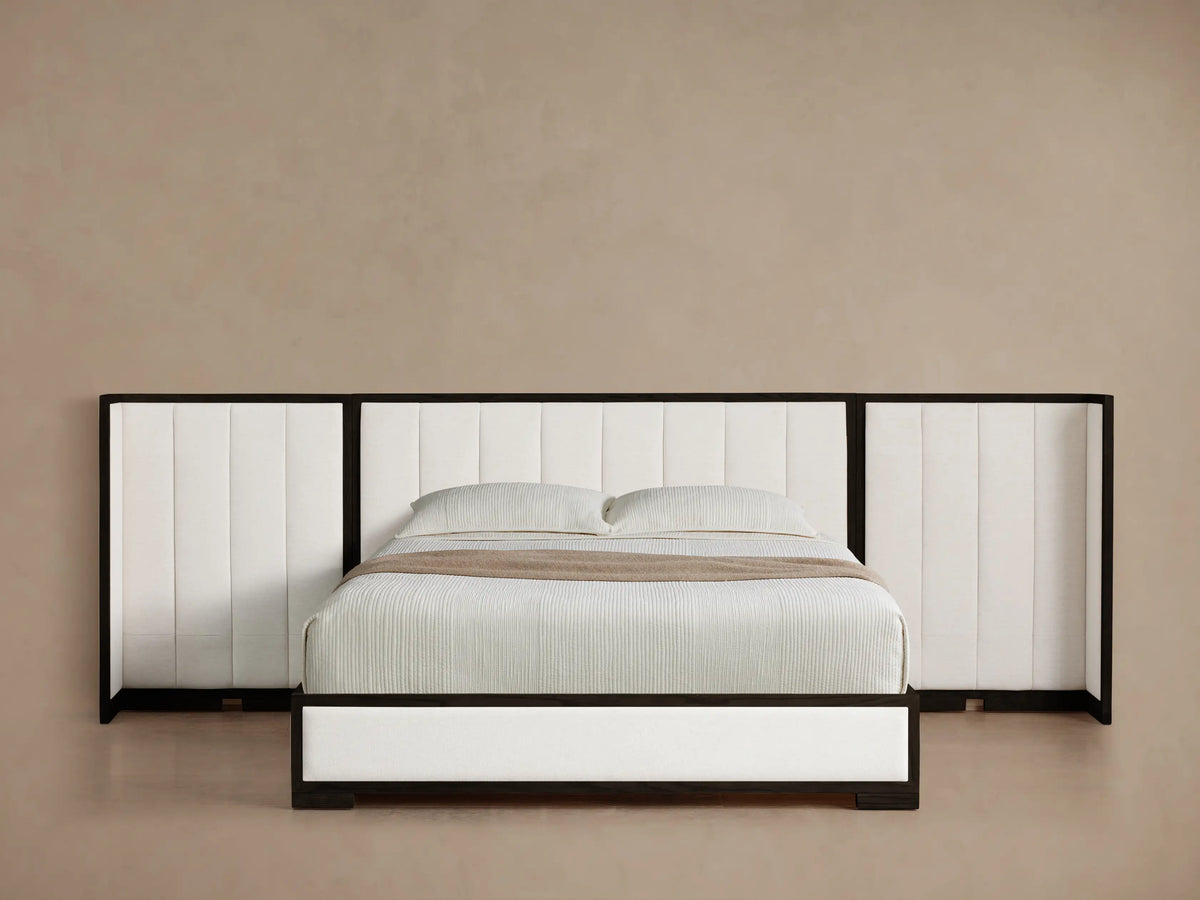 Darien Extended Channel-Stitched Shelter Bed. Black framed bed with white channel-stitched headboard extending left. White bedding on wood floor.