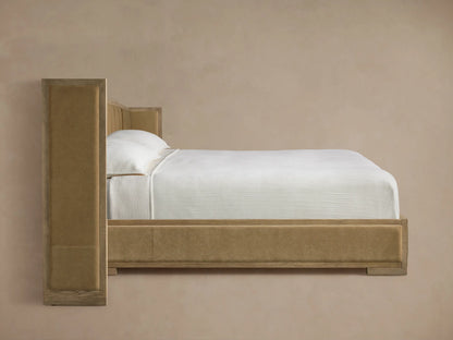 Close-up of a bed headboard with vertically paneled beige velvet upholstery framed by light brown wood with visible grain.