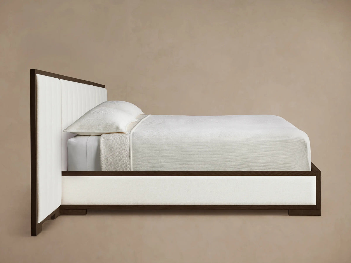 Side profile of the Darien Extended Channel-Stitched Panel Bed, dark brown oak frame, white channel-stitched panels, and white bedding.