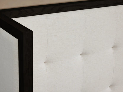 Darien Extended Box-Tufted Shelter Bed. White upholstered, dark wood bed with a wide, 3-panel, box-tufted headboard against a beige wall.