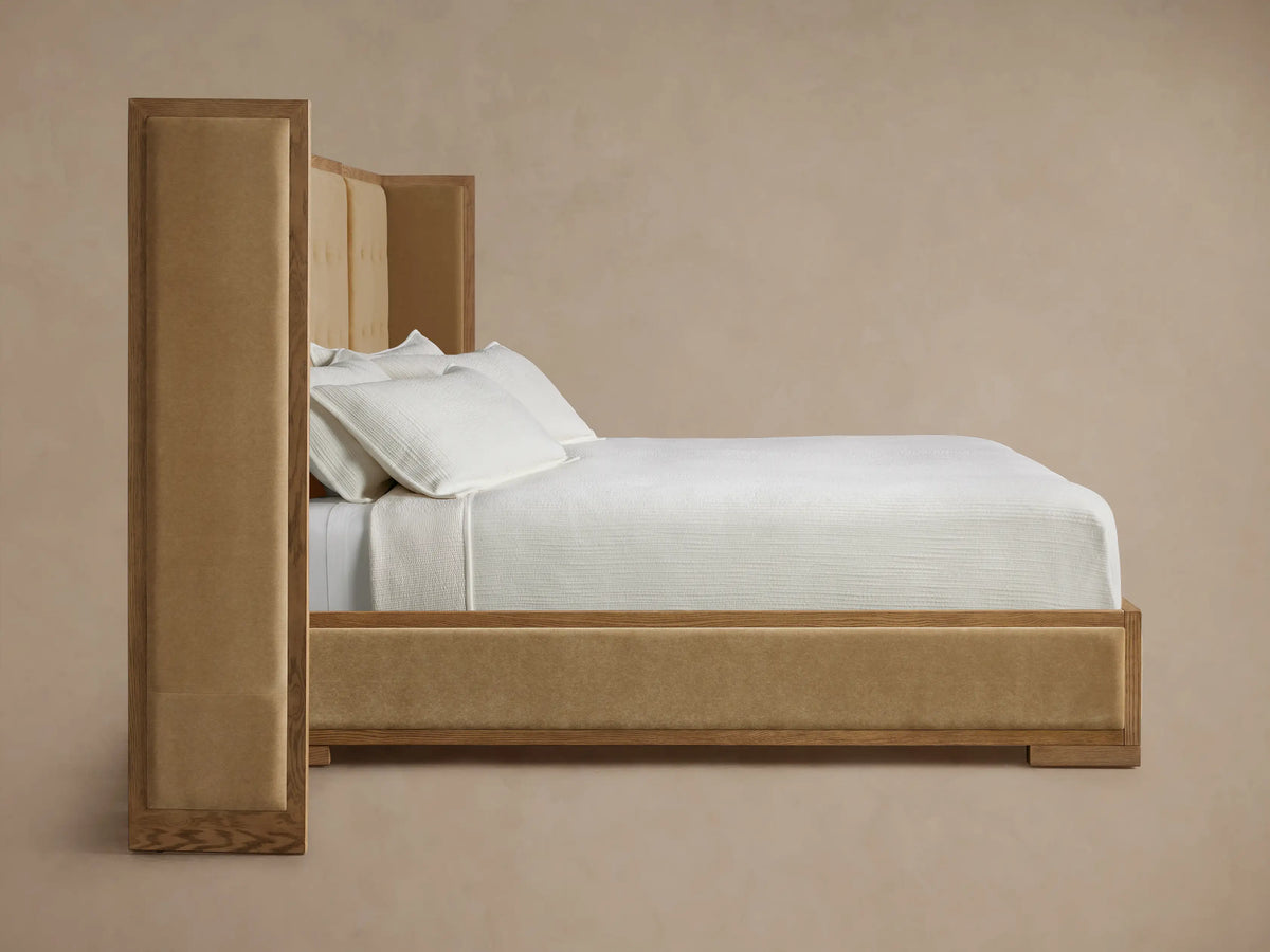 Angled view of Darien Extended Box-Tufted Shelter Bed. Light oak frame, tan upholstered box-tufted headboard, brown side panel.