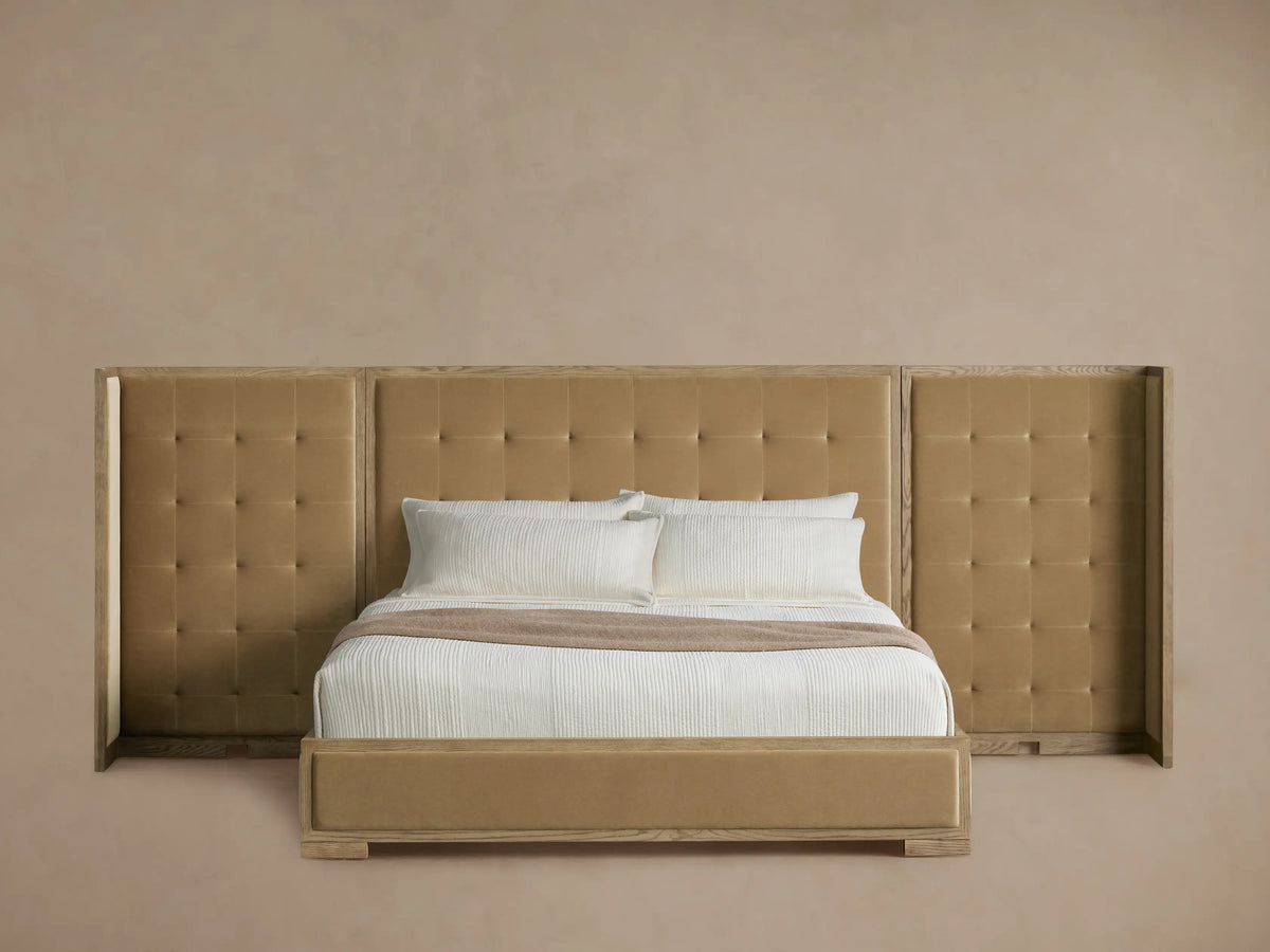 Tan upholstered Darien Extended Box-Tufted Shelter Bed, oak frame, with white bedding and throw blanket, angled view.