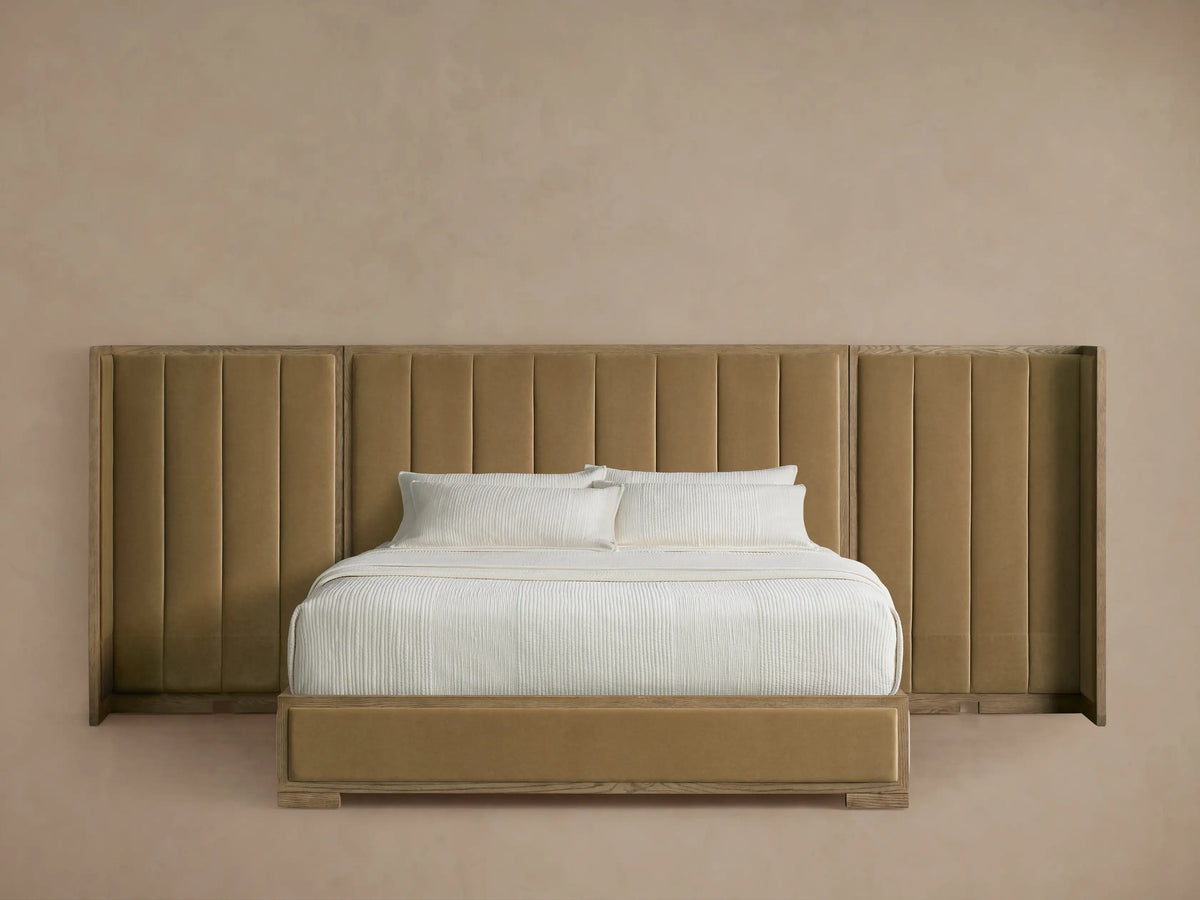 Tan upholstered bed with a tall, wide, channeled headboard and matching frame, dressed with white sheets and textured duvet.