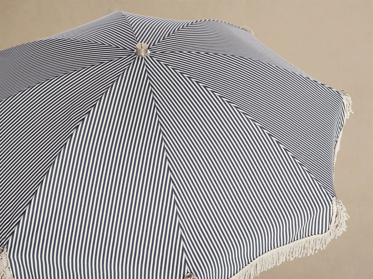 Interior view of a Beach umbrella with black and white vertical stripes, light fringed trim, and a natural wood pole.