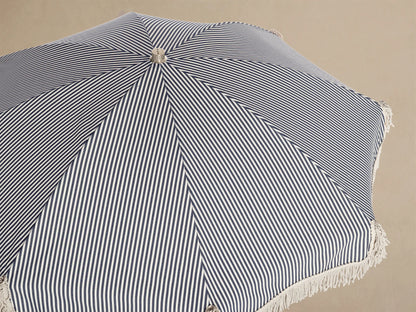 Interior view of a Beach umbrella with black and white vertical stripes, light fringed trim, and a natural wood pole.