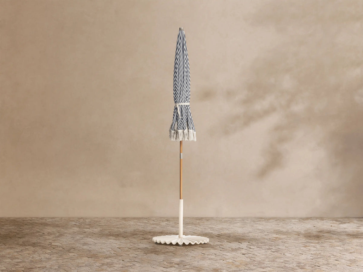 Close-up, elevated view of a navy blue and white striped beach umbrella with a silver finial and white fringe.