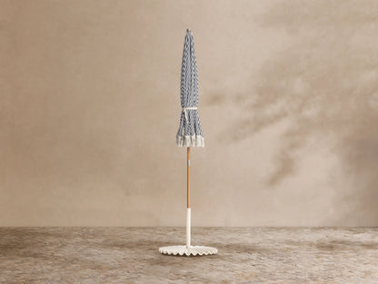 Close-up, elevated view of a navy blue and white striped beach umbrella with a silver finial and white fringe.
