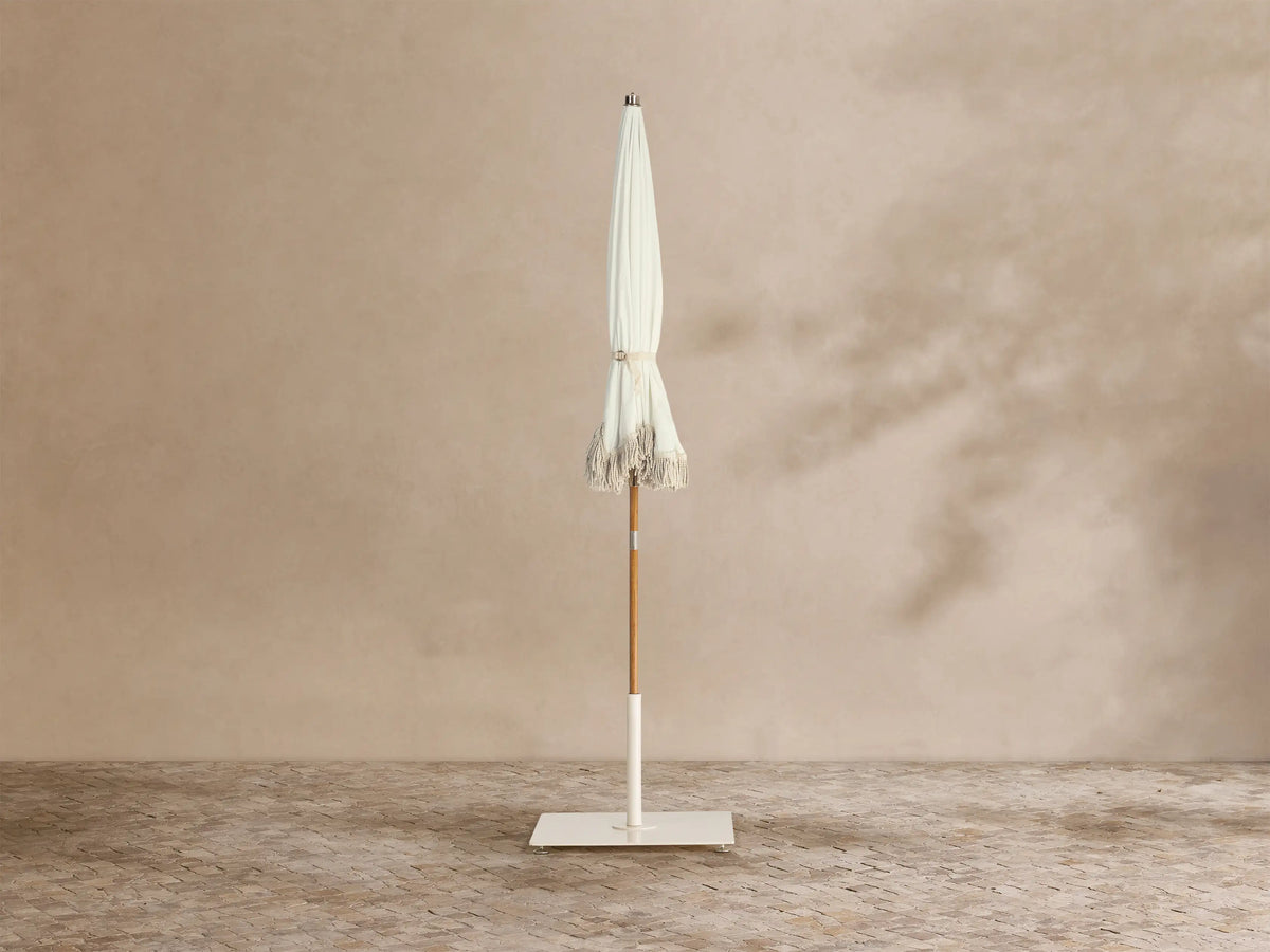 Interior view of a white umbrella with a light brown wooden pole, metal ribs, and scalloped edges trimmed with white fringe.