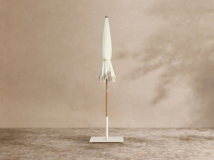 Interior view of a white umbrella with a light brown wooden pole, metal ribs, and scalloped edges trimmed with white fringe.